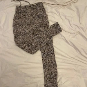 Leopardmönstrade byxor från Hollister - Snygga leopardmönstrade byxor från Hollister med ultra high-rise midja. Byxorna har en bekväm passform och dragsko i midjan för justerbarhet. Perfekta för en trendig look!