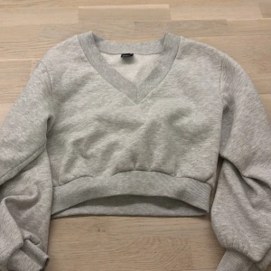 Grå croppad tröja från Gina Tricot - Säljer en stilren grå croppad tröja från Gina Tricot. Tröjan har en v-ringad design och långa ärmar med ribbade muddar. Perfekt för en avslappnad look. Hör av dig vid intresse! 😊