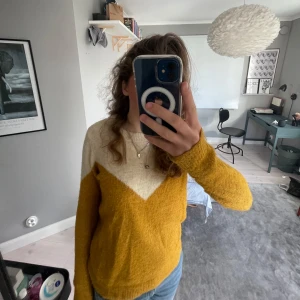 Gul och vit stickad tröja - Säljer en mysig gul och vit stickad tröja med ett V-format mönster framtill. Tröjan har långa ärmar och en rund halsringning. Lite nopprig