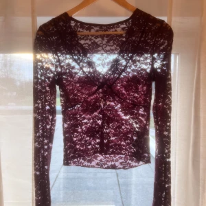 Vinröd spetsblus - Säljer en elegant vinröd spetsblus med långa ärmar och v-ringning. Blusen är genomskinlig och har ett vackert blommigt mönster. OBS den har 5 hål men man märker inte dom så mycket, två stora hål tre små❤️