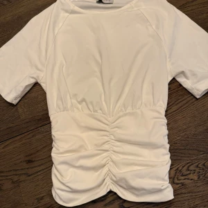 Vit kortärmad topp med rynkdetalj - Säljer en stilren vit topp från Anna Field med korta ärmar och en snygg rynkdetalj framtill❤️tveka inte att höra av dig! 