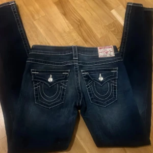 True religion jeans - Snygga true religion jeans med slitningar och kontrastsömmar. De har en femficksdesign och dekorativa bakfickor med knappar. Modellen är skinny 