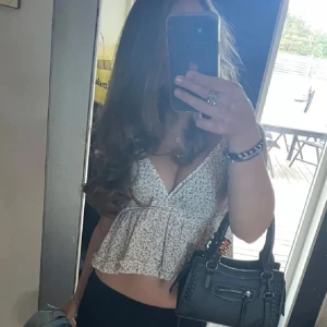 Blommig topp - Säljer en söt blommig croppad linnetopp med smala axelband och volangdetaljer. Perfekt för varma sommardagar. Toppen har en v-ringad design som ger en feminin look.