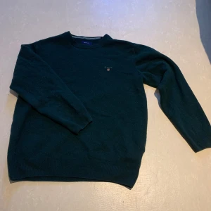 Mörkgrön ulltröja från GANT - Säljer en stilren mörkgrön tröja från GANT i superfin lammull. Tröjan har en liten broderad logga på bröstet och rund halsringning. Perfekt för kyligare dagar.