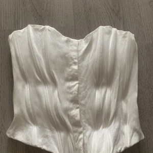 Vit korsett från Zara - Säljer en elegant vit korsett från Zara. Den har en stilren design med en glansig finish och är perfekt för att lyfta vilken outfit som helst. Korsetten är tillverkad i ett mjukt och bekvämt material🩷