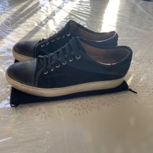 Svarta sneakers från Lanvin - Snygga svarta sneakers från Lanvin med snörning och vit sula. Perfekta för en stilren look. Kommer med og dustbag. Storlek UK9, Nypris 5000