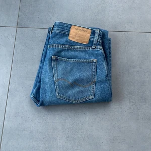 Blå jeans från Levi's - Säljer ett par klassiska blå jeans från Levi's. De har en rak passform och är tillverkade i slitstarkt denim. Perfekta för en avslappnad stil. Levi's-loggan syns tydligt på bakfickan.
