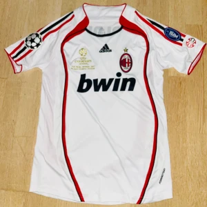 Retro Vit AC Milan fotbollströja med Maldini 3 - Säljer en vit AC Milan fotbollströja från Adidas med Maldini 3 på ryggen. Tröjan har röda och svarta detaljer samt korta ärmar. Champions League-märke på ärmen. Tröjan har aldrig använts och är i topp skick. 