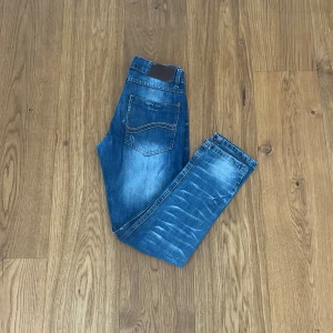 Blå jeansbyxor från Levis - Snygga blå jeansbyxor från Levis med en  femficksdesign och knappar i midjan. Byxorna har skuggningar och veckdetaljer för en trendig stil. Perfekta för en avslappnad vardagslook, men även för finare tillfällen. Jeansen är stora i storlek så de passar en storlek större. Vid funderingar är det bara att höra av sig! 