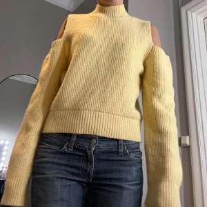 Gul stickad tröja med öppna axlar - Säljer en trendig gul stickad tröja med öppna axlar och hög krage. Perfekt för att hålla sig varm och stilren under kyligare dagar. Tröjan har långa ärmar och en ribbad struktur som ger en snygg passform. Passar perfekt till jeans eller kjol för en avslappnad look.