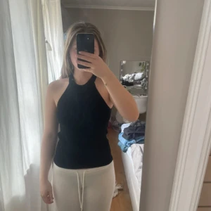 Svart ribbad ärmlös topp från Mango  - Säljer en stilren svart ribbad topp från Mango Den är ärmlös med en hög halsringning, perfekt för en chic och enkel look. Passar bra till både jeans och kjol. Hör av dig vid intresse!