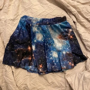 Galaxmönstrad kortkjol - Säljer en cool kortkjol med ett fantastiskt galaxmönster i blått och svart. Kjolen har en vid passform och är perfekt för att sticka ut med sin unika design. Materialet är mjukt och bekvämt. Står ingen storlek men gissar på XS/S