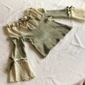 Grön tröja med spetsdetaljer från Emphasis - Säljer en unik grön tröja från Emphasis med vackra spetsdetaljer och knytband i grönt. Tröjan har långa ärmar med spets och volang vid ärmslut och hals. Perfekt för dig som vill ha något speciellt i garderoben!