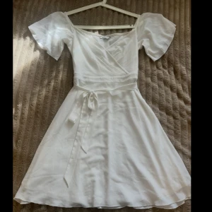 Vit klänning från NLY One - Säljer en söt vit klänning från NLY One med korta ärmar och knytband i midjan. Perfekt till studenten eller andra sommriga tillfällen. Klänningen har en v-ringad design och är gjord i ett lätt och luftigt material. Den är endast använd en gång vid min student. Inga skador eller missfärgningar. Hör av dig vid frågor!