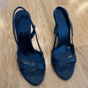 Svarta klackskor från Balenciaga - Snygga svarta klackskor från Balenciaga med en elegant design. Skorna har en smal rem över foten och en hög klack som ger en stilren look. Perfekta för att lyfta din outfit till nästa nivå. Klassiska svarta sandaletter!