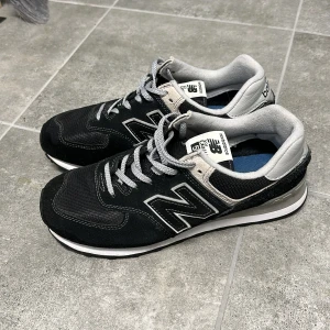 Svarta sneakers från New Balance - Snygga svarta sneakers från New Balance med grå detaljer och klassisk snörning. Skorna har en bekväm passform och är perfekta för vardagsbruk. Den ikoniska 'N'-loggan pryder sidan av skorna.