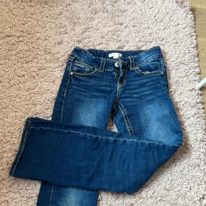 Low blå jeans från Gina Tricot - Snygga blå jeans från Gina Tricot med klassisk femficksdesign och knappgylf. Perfekta för en avslappnad stil. De har en bekväm passform och är tillverkade i ett slitstarkt denimtyg.
