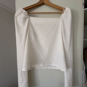 Vit långärmad blus från H&M - Säljer en stilren vit blus med långa ärmar från H&M. Tyget har en texturerad yta som ger en unik look. Perfekt för att klä upp eller ner beroende på tillfälle.