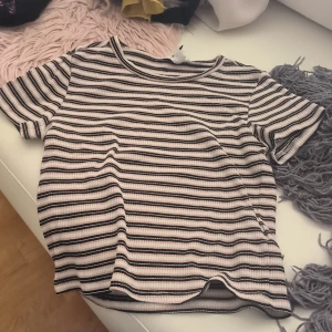 Randig ribbad topp från H&M Divided - Säljer en randig ribbad topp från H&M Divided i svart, vit och rosa. Toppen har korta ärmar och en rund halsringning. Perfekt för en avslappnad stil.