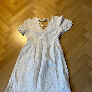 Vit klänning med broderade detaljer - Charmig vit klänning med v-ringning och korta ärmar. Klänningen har ett vackert broderat mönster och knytning i ryggen. Perfekt för sommarens varma dagar. Helt ny och enbart provad. Nypris 1200kr