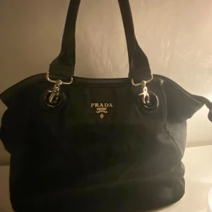 Svart väska  - Säljer en liknande och snygg svart axelväska med silverdetaljer. Väskan har två handtag och en dragkedja upptill. Och har en ficka på baksidan och får plats med dator, böcker och annat.