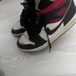 Säljer ett par klassiska Nike Air Jordans i svart, vitt och rött. Skorna har snörning och en ikonisk design (inte tvättade på bilden)
