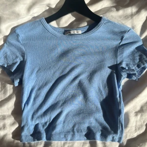 Blå kortärmad topp från Zara - Säljer en enkel och stilren blå topp från Zara. Den har en rund halsringning och korta ärmar, perfekt för en avslappnad look. Passar bra till jeans eller kjol för en casual stil. I storlek M men sitter mer som en S eller XS