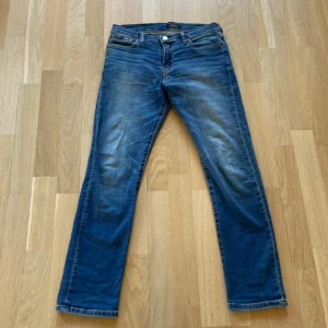 Blå jeans från Polo Ralph Lauren - Snygga blå jeans från Polo Ralph Lauren med klassisk femficksdesign och gylf. Perfekta för en avslappnad stil med en touch av elegans. Passar bra till både sneakers och kängor.