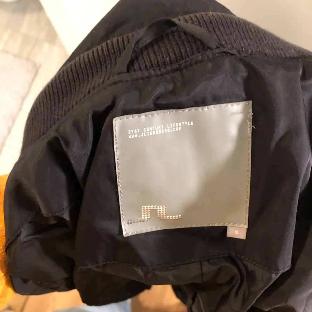 Säljer en stilren svart trenchcoat från J.Lindeberg. Jackan har ett bälte i midjan och långa ärmar. Perfekt för höst och vår med sin blandning av bomull och nylon. Den har knappar och en diskret design som passar till många tillfällen.. Takit.