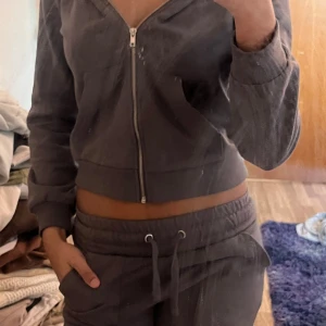 Grått mjukisset från lager157 - Säljer en stilren grå croppad hoodie med dragkedja framtill. Perfekt för en avslappnad look. Den har långa ärmar och ribbade muddar vid ärmslut och nederkant. Med matchande byxor. Kan säljas separat!