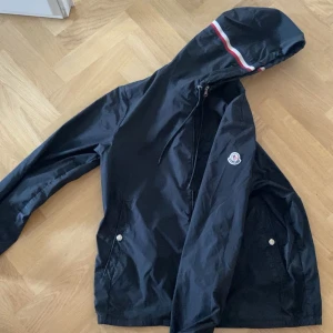 Svart vindjacka från Moncler - Säljer en stilren svart vindjacka från Moncler med huva och dragkedja. Jackan har långa ärmar och Moncler-logga på ärmen. Perfekt för blåsiga dagar. Nfc scan finns. Passar mig perfekt som är ca 190 lång ochh väger runt 75kg
