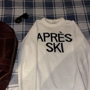 Vit stickad tröja med text - Säljer en vit stickad tröja med texten 'APRÈS SKI' i svart på framsidan. Tröjan har en rund halsringning och långa ärmar. Perfekt för kyliga dagar och mysiga stunder efter skidåkning.
