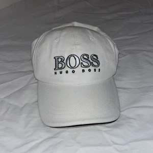 Hugo Boss keps - Snygg vit keps från Hugo Boss med broderad logga framtill. Perfekt för en stilren look. Justerbar rem baktill för optimal passform.