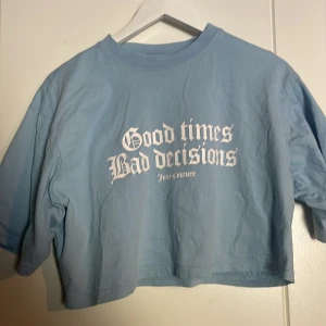 Blå croppad tränings t-shirt från Juicy Couture - Säljer en blå croppad t-shirt från Juicy Couture med texten 'Good times Bad decisions' tryckt på framsidan. T-shirten har en avslappnad passform och korta ärmar. Perfekt för en casual look!