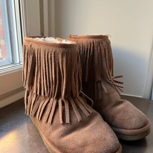 Bruna mockaboots med fransar - Säljer ett par bruna boots i mocka med fransar runt skaftet. De har en mjuk och varm insida, perfekt för kyligare dagar. Sulan är mönstrad för bra grepp.