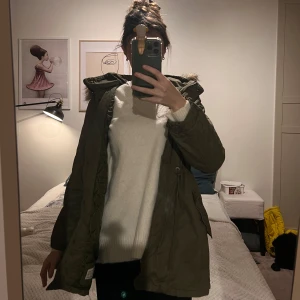 Olivgrön parkajacka med pälsdetalj - Säljer en olivgrön parkajacka med huva och pälsdetalj. Jackan har dragsko i midjan och stängs med dragkedja och knappar. Kommer passa en xs 