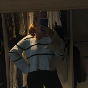 Vit stickad tröja med svarta ränder - Säljer en vit stickad tröja med svarta ränder. Tröjan har långa ärmar och en bred krage som ger en avslappnad look. 