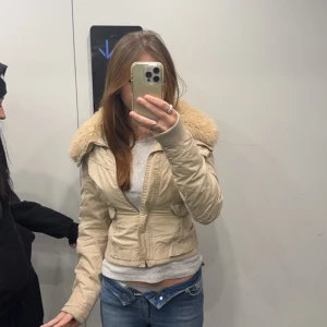 Pälsjacka  - Säljer en snygg beige jacka med pälsdetaljer på kragen. Jackan har dragkedja framtill och långa ärmar. Perfekt för kyligare dagar och ger en stilren look.