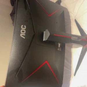 Svart AOC datorskärm - Säljer en svart AOC datorskärm med en elegant design och röda detaljer. Skärmen har en böjd form och står på ett stabilt stativ med tre ben. Perfekt för gaming eller arbete med hög upplösning.