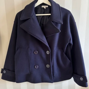 Marinblå kappa - Snygg mörkblå kappa från Designbysi med dubbelknäppning och två stora fickor. Jättefin till våren!! Jackan har använts en del, men det finns inga stora defekter🥰 Köpt för ca 700 men säljer för 350💗💗