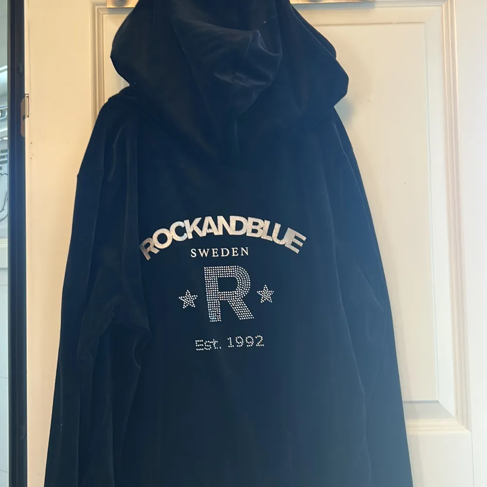 Säljer en svart hoodie från Rockandblue med dragkedja och huva. Tröjan har ett snyggt tryck på ryggen med texten 'ROCKANDBLUE SWEDEN' och stjärnor. Perfekt för en avslappnad stil.. Neuletakit & Villapaidat.