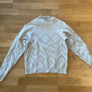 Vit stickad tröja med mönster - Säljer en stilren vit stickad tröja med ett dekorativt hålmönster. Tröjan har långa ärmar och en hög krage som ger en elegant look. Stl S men den är liten i storleken så passar xs 
