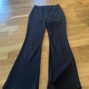 Svarta utsvängda byxor - Snygga svarta byxor med utsvängda ben. Perfekta för en stilren look. Byxorna har en hög midja och är gjorda i ett mjukt material som ger en bekväm passform. Har ett liten tråd som har släppt på knät se andra bild. 