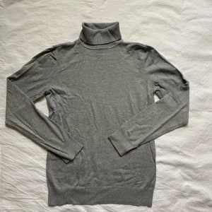 Grå polotröja från Stockh LM - Säljer en stilren grå polotröja från Stockh LM. Tröjan har långa ärmar och en klassisk polokrage. Den är tillverkad i ett mjukt material som ger en bekväm passform.