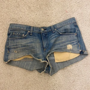 Blå jeansshorts från Rag & Bone - Säljer ett par coola blå jeansshorts från Rag & Bone. De har en fransig kant och slitna detaljer för en avslappnad look. Perfekta för sommardagar! 