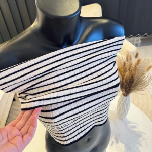 Randig offshoulder topp - Snygg randig offshoulder topp i svart och beige. Denna ribbade topp har en stilren design med horisontella ränder och en tight passform. Perfekt för att ge din outfit en trendig touch. Passar bra i m/l storlek. Jag rekommenderar den varmt.🌸👌