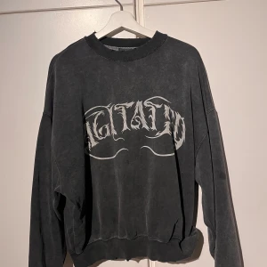 Svart sweatshirt från Pull&Bear - Säljer en mörkgrå sweatshirt från Pull&Bear med ett tryck där de står ”AGITATED” fram. Jag har använt den väldigt lite men haft den ett tag.  Den är luddig inuti och kan därför ludda av sig lite på vita tröjor som man har under. Priset är rörligt vid snabb och bra affär! 