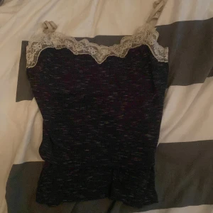 Svart linne med spetsdetaljer - Snyggt svart linne med spetsdetaljer vid halsringningen. Perfekt för en stilren look. Axelbanden är smala och ger en elegant touch.