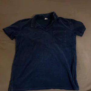 Mörkblå frotté skjorta - Säljer en mörkblå frotté skjorta i storlek 158/164. T-shirten har en bröstficka och korta ärmar, perfekt för en avslappnad stil. Tillverkad i ett mjukt material som känns skönt mot huden.