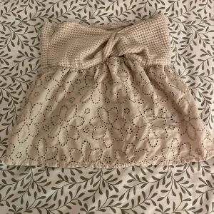 Beige kjol med spetsdetaljer - Charmig beige kjol med en stickad midja och vackra spetsdetaljer i blommönster. Kjolen har en volangliknande design och är perfekt för en somrig look.